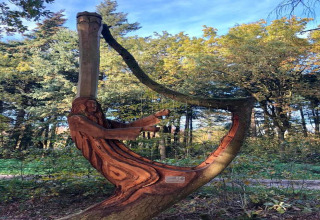 Scultura in legno di un uomo che suona l'arpa, intagliata artisticamente in un albero vicino a uno chalet.