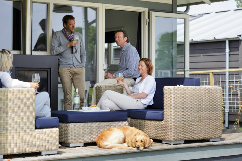Cuatro adultos y un perro se relajan con vino en la terraza de un chalet durante el día.