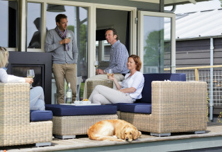 Cuatro adultos y un perro se relajan con vino en la terraza de un chalet durante el día.