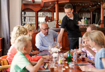 Een gezin dineert samen in een chaletrestaurant, terwijl een ober drankjes aan tafel serveert.