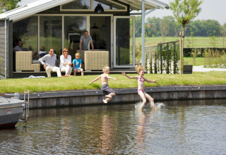 Zwei Kinder springen ins Wasser vor einem Chalet, während die Familie entspannt auf der Terrasse sitzt.