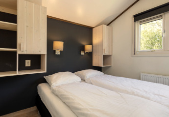 Slaapkamer met twee aparte bedden, wit beddengoed, wandkasten en raam in chalet Water park Terkaple 1 in Nederland.