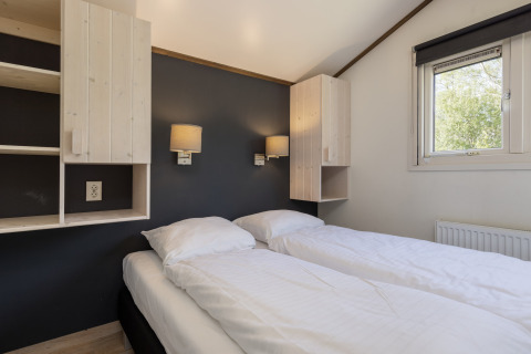 Chambre avec deux lits simples, draps blancs, armoires murales et fenêtre au chalet Water park Terkaple 1 aux Pays-Bas.