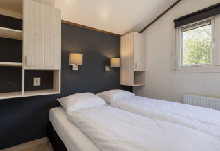 Chambre avec deux lits simples, draps blancs, armoires murales et fenêtre au chalet Water park Terkaple 1 aux Pays-Bas.