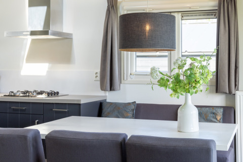 Cocina y comedor de chalet moderno con sofá gris, mesa blanca y jarrón de flores verdes en Terkaple.