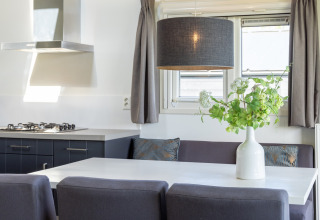 Modernes Chalet mit Essbereich, grauem Sofa, weißem Tisch, Pflanzenvase und großen Fenstern in Terkaple.