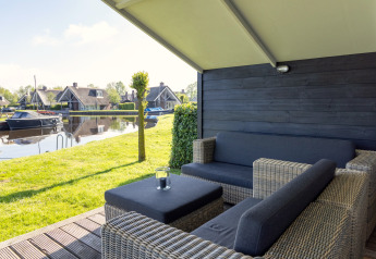 Overdekt terras bij chalet Water park Terkaple 1, uitkijkend op water en tuin in Nederland.