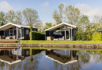 To moderne chalets ved vandet i Water park Terkaple 1, Holland, med træer og klart spejlbillede.