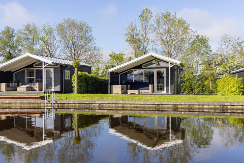 Two modern chalets on the waterfront at Water park Terkaple 1, Netherlands, reflected in calm water.