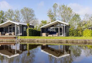 Two modern chalets on the waterfront at Water park Terkaple 1, Netherlands, reflected in calm water.