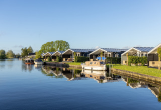 Chalets junto al agua en Water park Terkaple 1 en los Países Bajos con barcos amarrados al muelle.