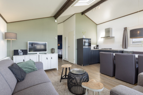 Moderne stue og køkken i Water park Terkaple 1-chalet med grå sofa, spiseplads og lyst interiør.