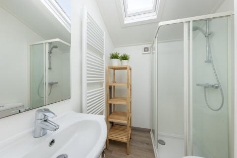 Salle de bain moderne avec douche, lavabo blanc, étagère en bois et puits de lumière à Water park «Terkaple 1».