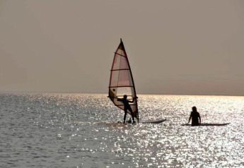 Twee personen windsurfen en peddelen op het meer bij chalet Water park «Terkaple 1» in Nederland bij zonsondergang.