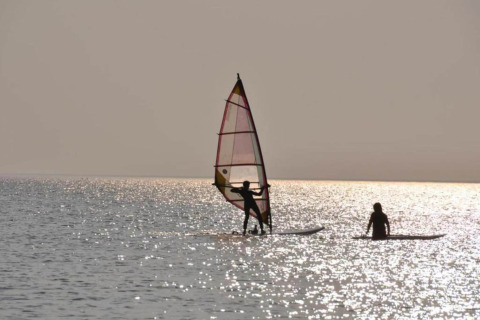 Dos personas haciendo windsurf y remo en el lago junto al chalet Water park «Terkaple 1» en los Países Bajos al atardecer.