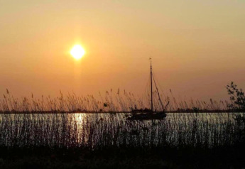 Sunset over the lake at Water park Terkaple 1 in the Netherlands, sailboat and reeds in silhouette.