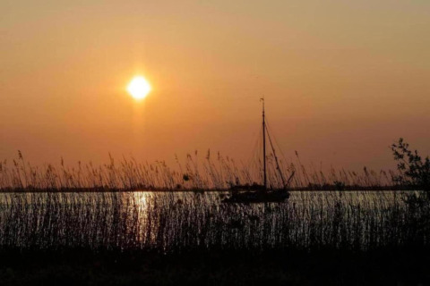 Sunset over the lake at Water park Terkaple 1 in the Netherlands, sailboat and reeds in silhouette.