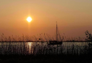 Sunset over the lake at Water park Terkaple 1 in the Netherlands, sailboat and reeds in silhouette.