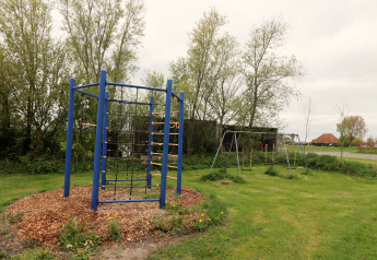 Speeltuin met schommels en klimrek bij Cosy cabin 1 in Nederland, omgeven door gras en bomen.