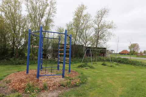 Aire de jeux avec balançoires et structure d’escalade à Cosy cabin 1 aux Pays-Bas, entourée d’arbres.