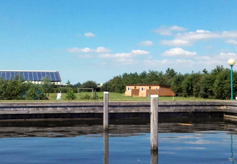 Charmant chalet au bord d’un lac avec pelouse, arbres et panneaux solaires à l’arrière aux Pays-Bas.