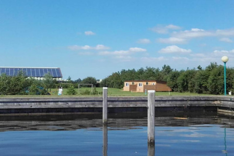 Charmant chalet au bord d’un lac avec pelouse, arbres et panneaux solaires à l’arrière aux Pays-Bas.