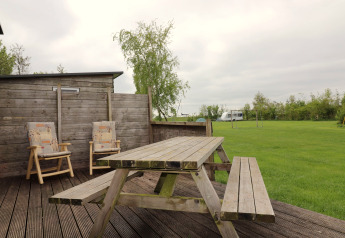 Terrasse extérieure de Cosy cabin 1 aux Pays-Bas avec table en bois, chaises et pelouse verte.