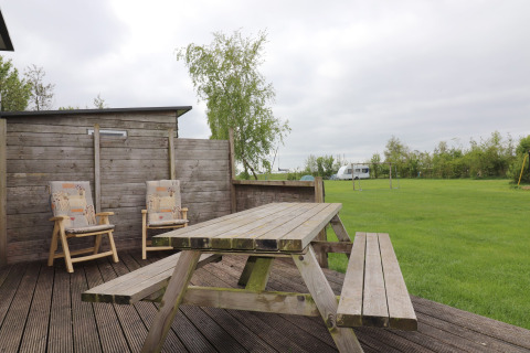 Terrasse extérieure de Cosy cabin 1 aux Pays-Bas avec table en bois, chaises et pelouse verte.