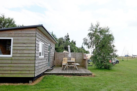 Cabane en bois cosy avec terrasse, table de pique-nique et chaises sur pelouse aux Pays-Bas.