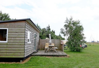 Cabane en bois cosy avec terrasse, table de pique-nique et chaises sur pelouse aux Pays-Bas.