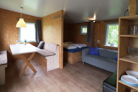 Vue intérieure de Cosy Cabin 1 aux Pays-Bas, avec table à manger, canapé, lit et fenêtres.