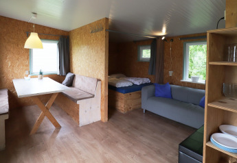 Vista del interior de Cosy Cabin 1 en Holanda, con mesa de comedor, sofá, cama y ventanas grandes.