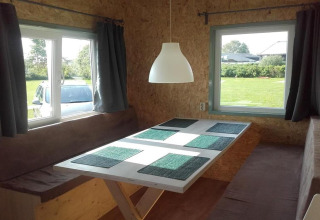 Coin repas dans une cabane douillette avec bancs marron, table blanche et fenêtres aux Pays-Bas.