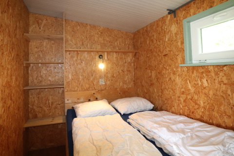 Petite chambre chaleureuse de Cosy cabin 1 aux Pays-Bas avec murs en bois et deux lits simples.