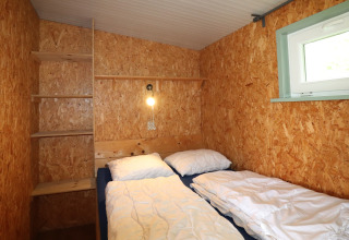 Petite chambre chaleureuse de Cosy cabin 1 aux Pays-Bas avec murs en bois et deux lits simples.