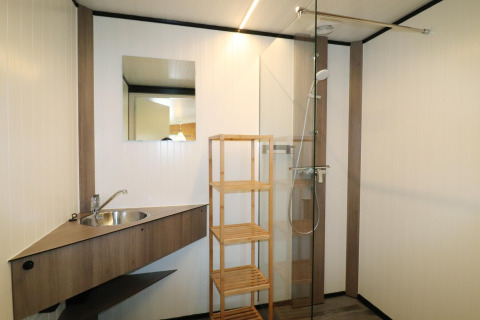 Salle de bain moderne du Cosy Cabin 1 aux Pays-Bas, avec douche, lavabo, étagère en bois et miroir.