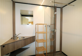 Salle de bain moderne du Cosy Cabin 1 aux Pays-Bas, avec douche, lavabo, étagère en bois et miroir.