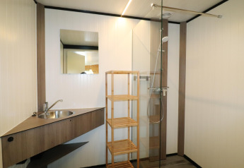 Salle de bain moderne du Cosy Cabin 1 aux Pays-Bas, avec douche, lavabo, étagère en bois et miroir.