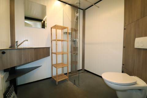 Salle de bain moderne avec détails en bois, douche, lavabo, étagère et WC à Cosy cabin 1 aux Pays-Bas.