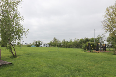 Terrain de camping vert à Cosy cabin 1 aux Pays-Bas, avec aire de jeux, tente, caravane et arbres.