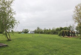 Terrain de camping vert à Cosy cabin 1 aux Pays-Bas, avec aire de jeux, tente, caravane et arbres.