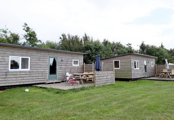 Vista de dos cabañas de madera con zona de estar exterior en Cosy cabin 1, Países Bajos, césped al frente.