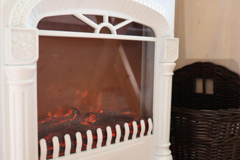 Gros plan sur une cheminée électrique blanche et un panier sombre dans la Cosy cabin 1 aux Pays-Bas.