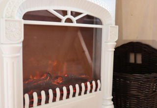 Gros plan sur une cheminée électrique blanche et un panier sombre dans la Cosy cabin 1 aux Pays-Bas.