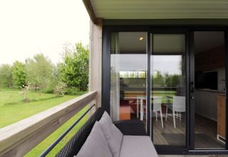 Vue depuis la terrasse du chalet Terrace lodge 2 aux Pays-Bas, canapé extérieur et porte-fenêtre vitrée.