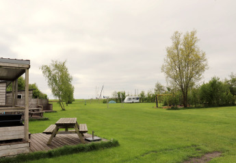 Groen grasveld met picknicktafels, bomen en caravan bij chalet "Terrace lodge 2" in Nederland.