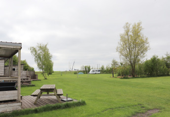 Grüne Wiese mit Picknicktisch, Bäumen und Wohnwagen bei „Terrace lodge 2“ in den Niederlanden.
