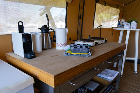 Küchenbereich im Safarizelt mit Kaffeemaschine, Wasserkocher, Herdplatte und Handtüchern.