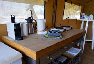 Küchenbereich im Safarizelt mit Kaffeemaschine, Wasserkocher, Herdplatte und Handtüchern.