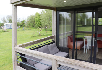 Terrasse mit Sitzbank und Blick ins Wohnzimmer im Terrace lodge 2 auf einem grünen Campingplatz in den Niederlanden.